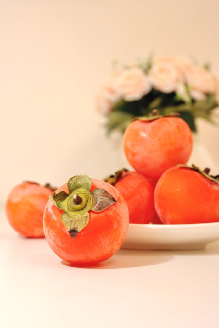 Photo by Jimmy Wu a white plate topped with tomatoes next to a vase of flowers