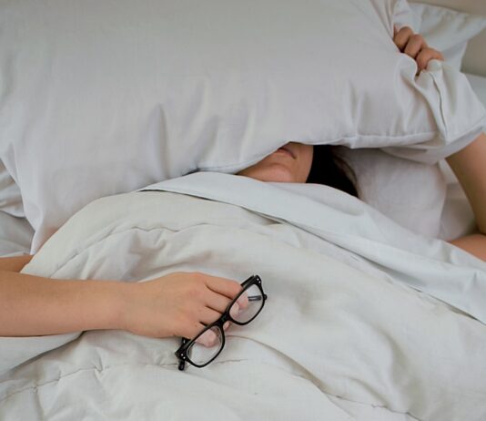 뱃살 타파의 신비, 수면의 역할 person lying on bed while covering face with pillow and holding eyeglasses