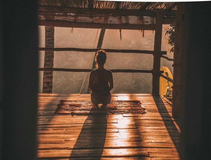 Photo by Jared Rice woman meditating on floor with overlooking view of trees